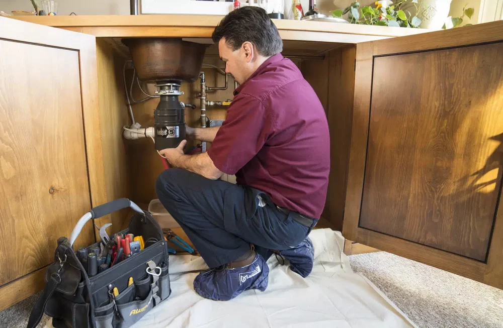 Plumber installing garbage disposal in residential home in Warrenton, VA.